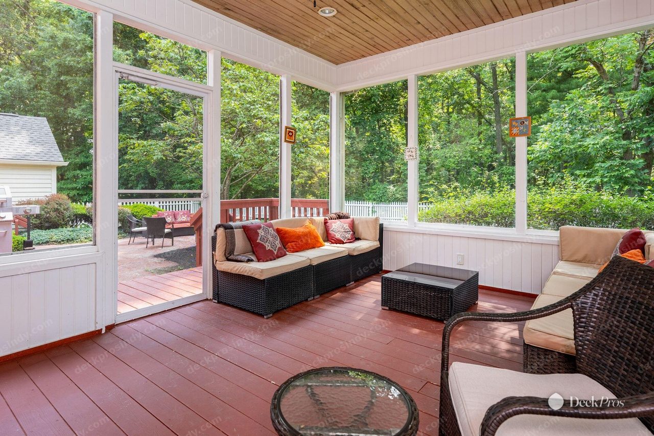The Anderson screened porch before work: a rust-red painted floor under white beadboard walls and a natural wood ceiling, looking out to woods.