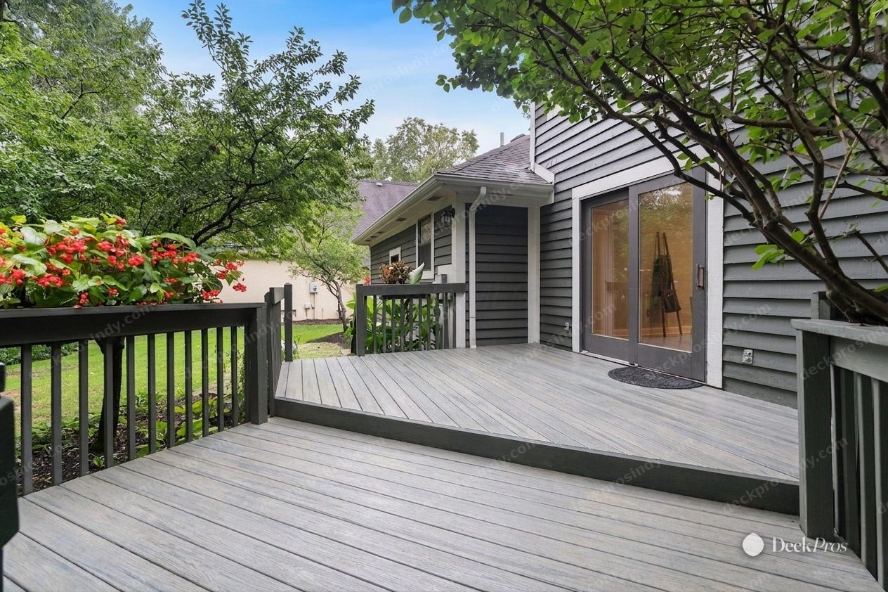 The same deck after: Trex Enhance Naturals decking in Foggy Wharf, a driftwood grey with a picture-frame border and no visible screws, against the grey siding and the red-berried shrub.