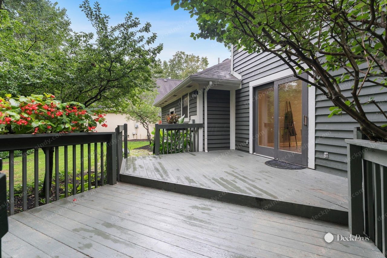 The Douglas deck before work: grey-green painted boards worn through in patches, with matching painted railing, outside the sliding patio door.