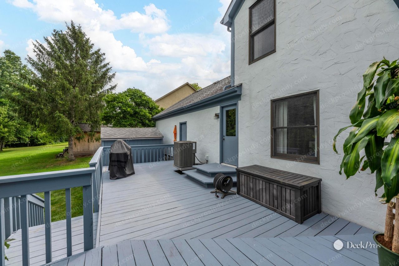The Spears wrap-around deck before work: grey-painted boards and a blue-grey painted railing running along the white stucco house, with a storage bench and air-conditioning unit.